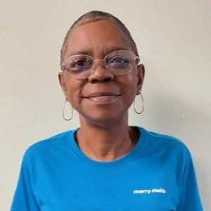 smiling woman with a blue merry maids uniform standing in front of a tan wall